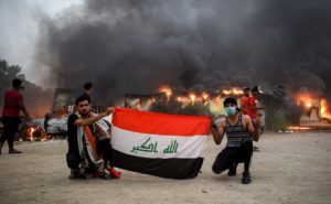 Iraqi protesters pose with a national flag during an anti-government demonstration outside the burning local government headquarters in Nasiriyah. (AFP)