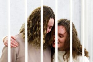 Belsat TV journalists Katerina Bakhvalova (R) and Daria Chultsova (L), who were detained in Nov 2020 while reporting on anti-government protests, embrace each other in a defendants' cage before the start of their trial in Minsk. (File photo: AFP)
