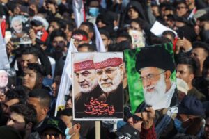 Iraqi demonstrators lift a placards depicting Iraqi commander Abu Mahdi al-Muhandis (C) and Iranian Revolutionary Guards commander Qasem Soleimani (L) and Iran's Supreme Leader Ayatollah Ali Khamenei (R), in Tahrir square in the capital Baghdad on January 3, 2021. (AFP)