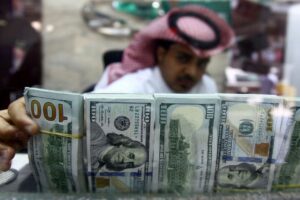 A Saudi money changer, pictured through a glass, arranges U.S banknotes at a currency exchange shop in Riyadh. (Reuters)