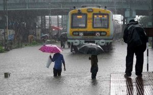 People cross inundated railway tracks next to a parked passenger train during heavy monsoon rains in Mumbai, India, June 9, 2021. REUTERS
